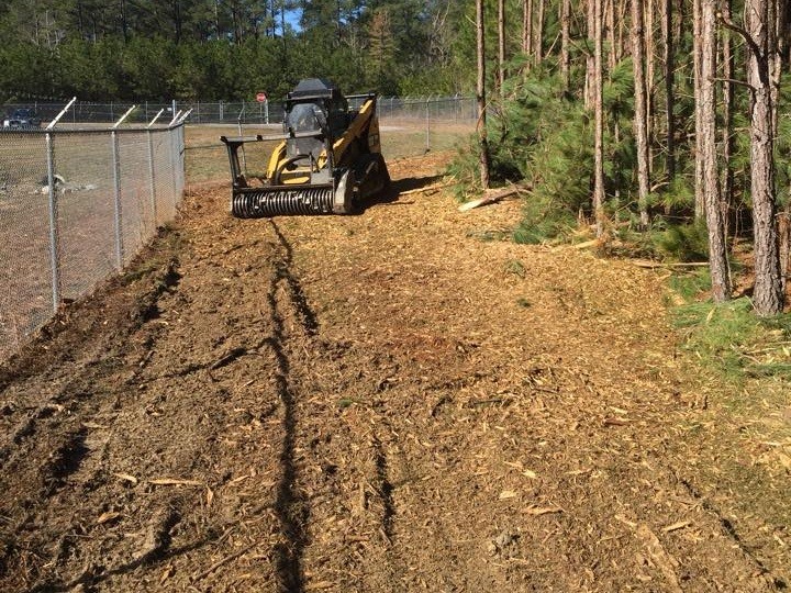 Skid Steer breaking debris on path in between fence and forest